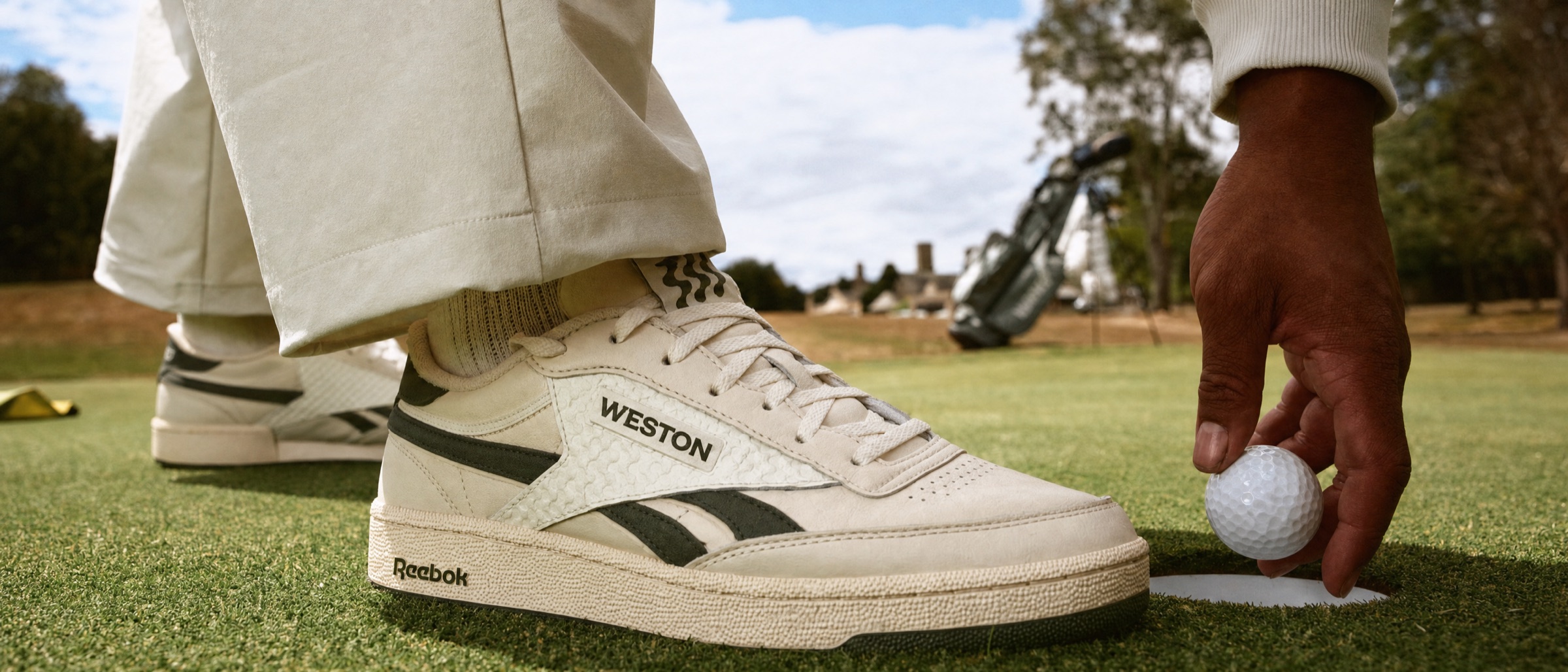 The Court Golf Shoe in Legacy Green at the hole, a ball set down by hand, the clubhouse beyond.