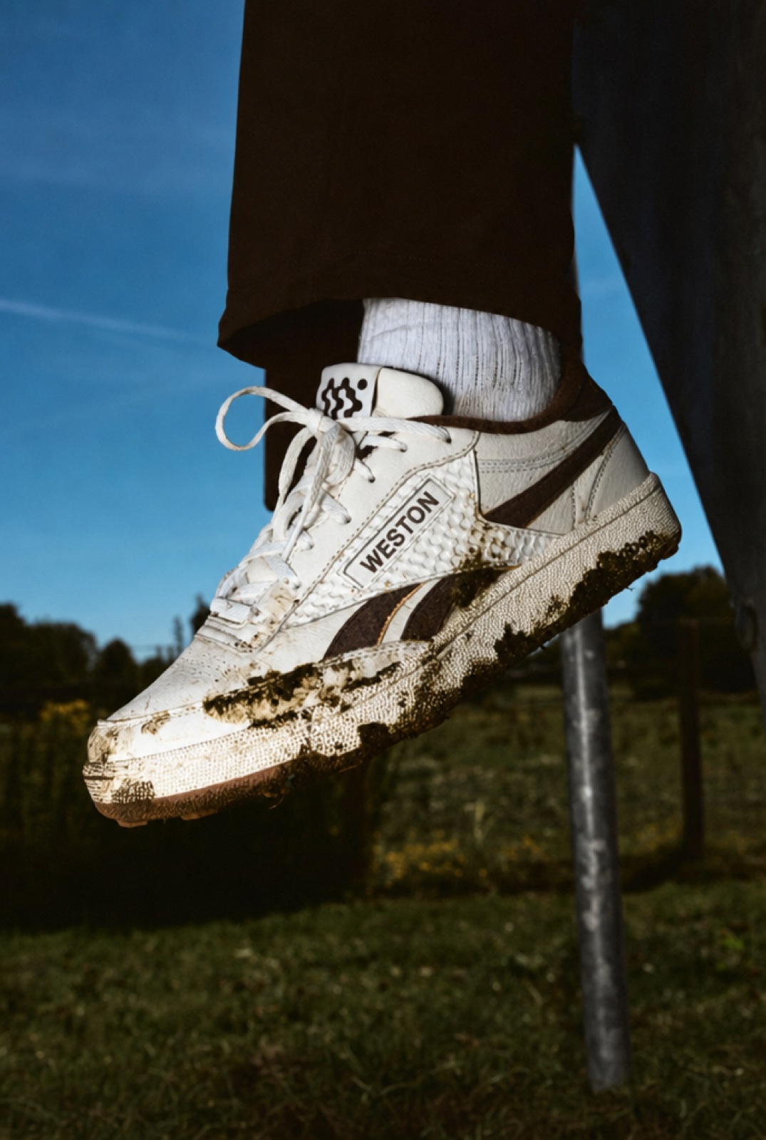 A mud-splashed Court Golf Shoe against a deep blue sky.